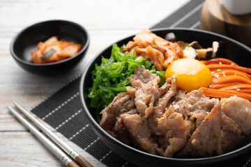 Kimchi fried rice with fried brisket and wakame seaweed and raw egg in black bowl on wooden table,(bibimbap).