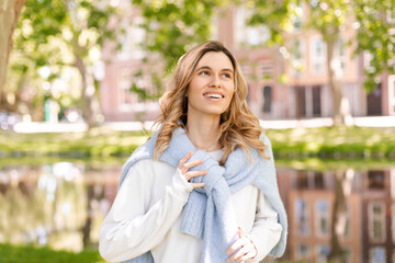 Beautiful woman smiling and look at camera at park at sunny day. Outdoor portrait of a smiling curly blonde girl. Happy cheerful girl laughing at park, look at side, touch sweater, show toothy smile.