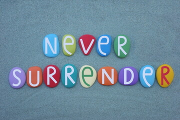Fototapeta na wymiar Never surrender, motivational message composed with multi colored stone letters over green sand