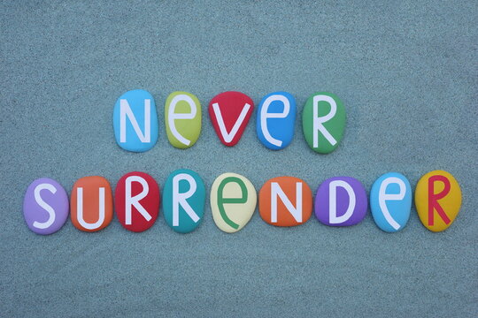 Never surrender, motivational message composed with multi colored stone letters over green sand