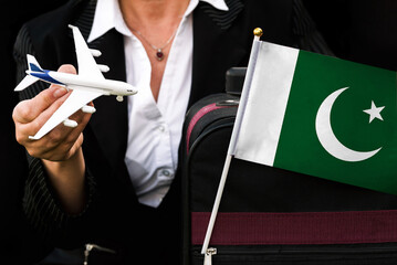 business woman holds toy plane travel bag and flag of Pakistan

