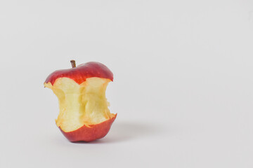 A portion of the red apple was eaten, laying on the white floor.