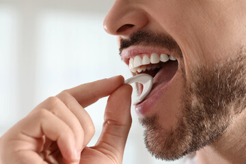 Man putting chewing gum into mouth on blurred background, closeup