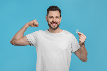 Happy man holding condom on light blue background