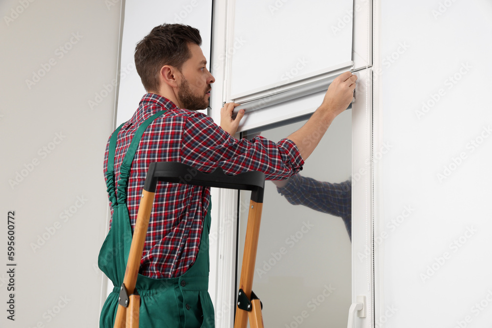 Poster Worker in uniform installing roller window blind indoors