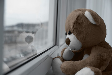 Cute lonely teddy bear on windowsill indoors, closeup. Space for text