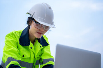 Close-up face of A surveying female electrical engineer wearing glasses is using a laptop computer and planning the construction of a high-voltage pylon.