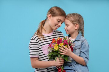 Fototapeta na wymiar Little daughter congratulating her mom with flowers on light blue background. Happy Mother's Day
