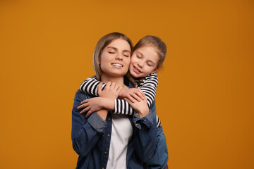 Little daughter hugging her mom on orange background. Happy Mother's Day