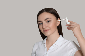 Obraz premium Young woman using ear spray on light grey background. Space for text