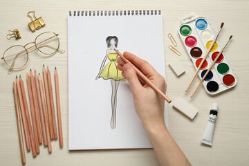 Fashion designer creating new look. Woman drawing sketch in pad with pencil at white wooden table,...