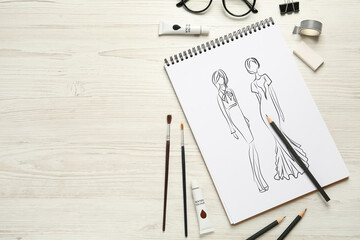 Sketches of different clothes in pad on white wooden table, space for text. Fashion designer's desk with stationery, flat lay