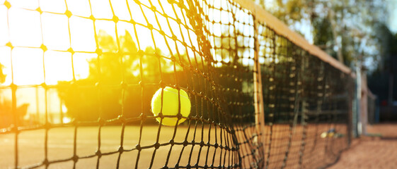 Bright yellow tennis ball hitting into net outdoors on sunny day, banner design