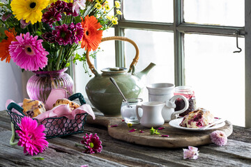 A rustic window setting of tea and scones with a vase of colourful flowers. - obrazy, fototapety, plakaty