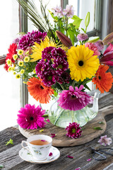 A bright beautiful colourful flower arrangement with a cup of tea in front.