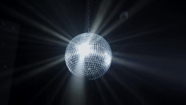 Disco Ball with Reflected Moving Rays Rotating. Mirror disco ball in white light. Isolated disco ball on black background. Close-up. Mirror ball spinning indoors. Performance. The reflection of lights