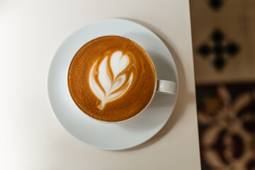 Delicious hot cappuccino with beautiful latte art in a white mug. Aromatic coffee with milk, top view