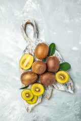 Halved ripe yellow kiwi fruit on a wooden board on a light background, vertical image. top view. place for text