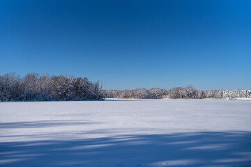 open snowy view across a frozen country lake with trees on the shore