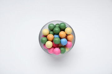Bowl with many bright gumballs on white background, top view