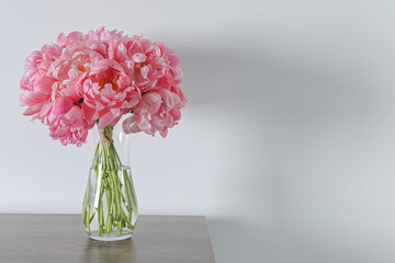 Beautiful bouquet of pink peonies in vase on wooden table against white background. Space for text