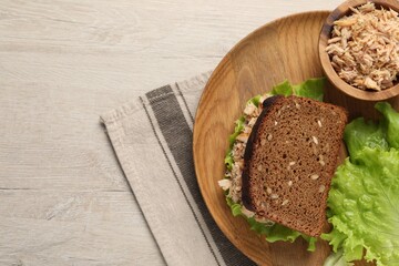 Delicious sandwich with tuna and lettuce leaves on white wooden table, top view. Space for text