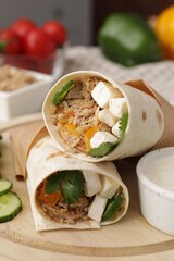 Delicious tortilla wraps with tuna and vegetables on wooden board, closeup