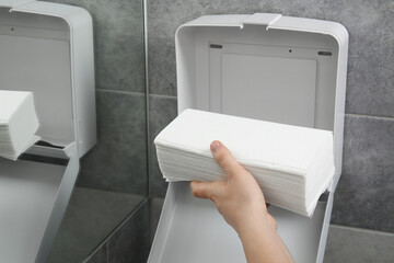 Woman putting new fresh paper towels into dispenser in bathroom, closeup