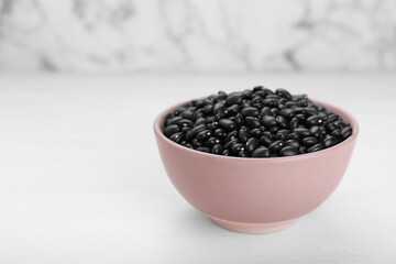 Fototapeta na wymiar Bowl of raw black beans on white wooden table. Space for text