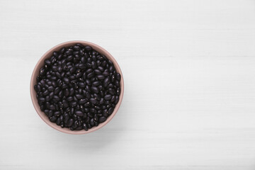 Fototapeta na wymiar Bowl of raw black beans on white wooden table, top view. Space for text