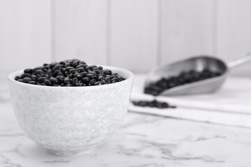 Fototapeta na wymiar Bowl of raw black beans on white marble table. Space for text