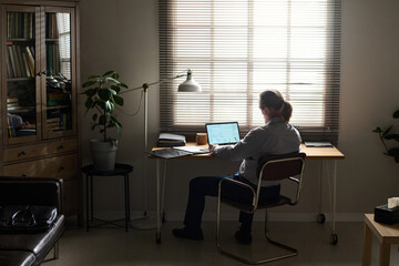 Fototapeta premium Back view of mature male psychologist sitting in front of laptop by his workplace in office and waiting for next patient in trouble