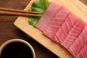 Tasty sashimi (pieces of fresh raw tuna), lettuce, soy sauce and chopsticks on wooden board, flat...