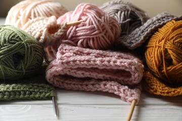 Balls of soft yarns, knitting and needles on white wooden table, closeup