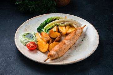 Chicken shish kebab with potato wedges, tomatoes, sauce and greens in plate.