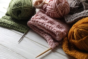Balls of soft yarns, knitting and needles on white wooden table