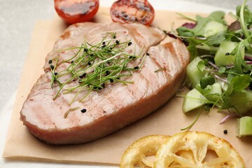 Delicious tuna steak, salad and lemon on parchment paper, closeup