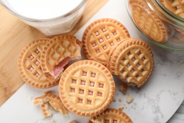 Tasty sandwich cookies with cream and glass of milk on white marble board, flat lay