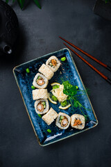 Japanese sushi roll set with shrimps tempura, cucumber, onion, green peas, ginger and wasabi with chopsticks.