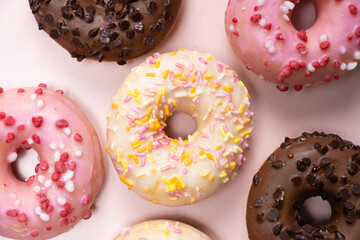 Lots of little donuts with white, pink and chocolate glaze on a pink background, top view