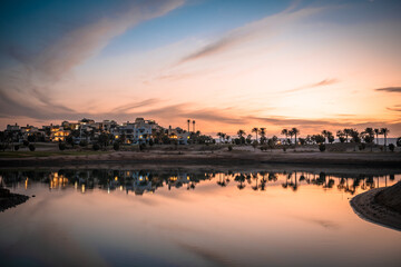 Sonnenuntergang an der Lagune bei Ancient Sands in El Gouna, &Auml;gypten. Die LAndschaft mit den Plamen und H&auml;usern spiegelt sich im Wasser.