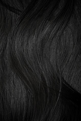 Brunette or black hair. Female long dark hair in black. Beautifully laid curls. Closeup texture in a dark key. Hairdressing, hair care and coloring. Shading gray hair. Background with copy space.
