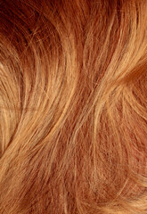 Red hair close-up as a background. Women's long orange hair. Beautifully styled wavy shiny curls. Hair coloring bright shades. Hairdressing procedures, extension.