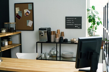 Workplace of waitress or clerk of modern cafe with computer monitor standing on counter desk against shelves with jars and other stuff
