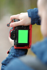 A close up view of a man holding vertically a camera with a green screen.