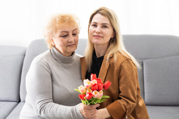 Happy mother's day. Beautiful young woman and her mother with flowers at home.