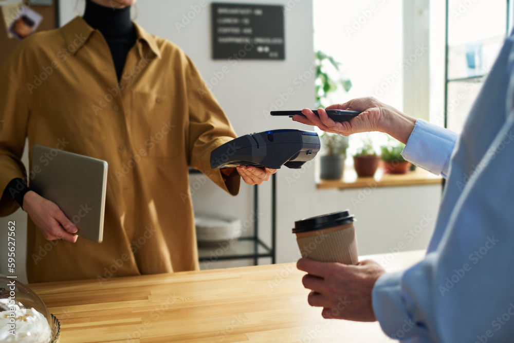 Poster close-up of clerk with terminal over counter desk and female client with smartphone during contactle