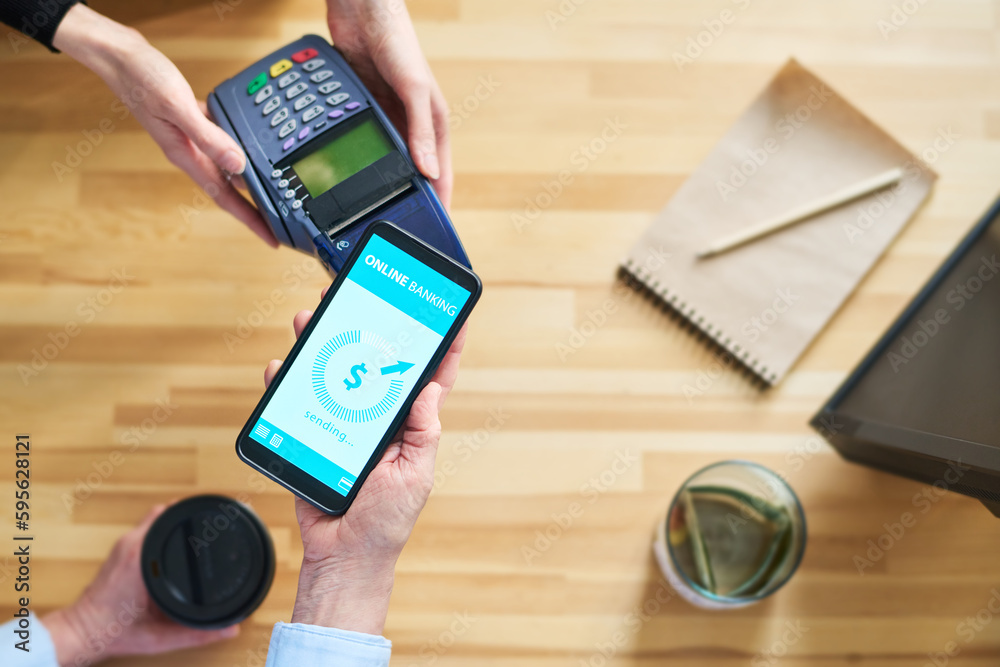 Aufkleber Top view of hands of clerk with terminal and client with smartphone over counter desk during contactless payment for food and drinks