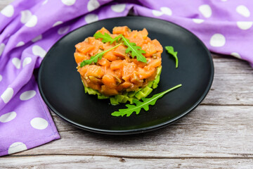 Salmon tartare with arugula on a wooden background