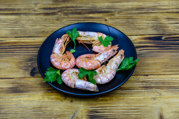 Fototapeta na wymiar Plate with prepared shrimps and parsley leaves on a wooden table